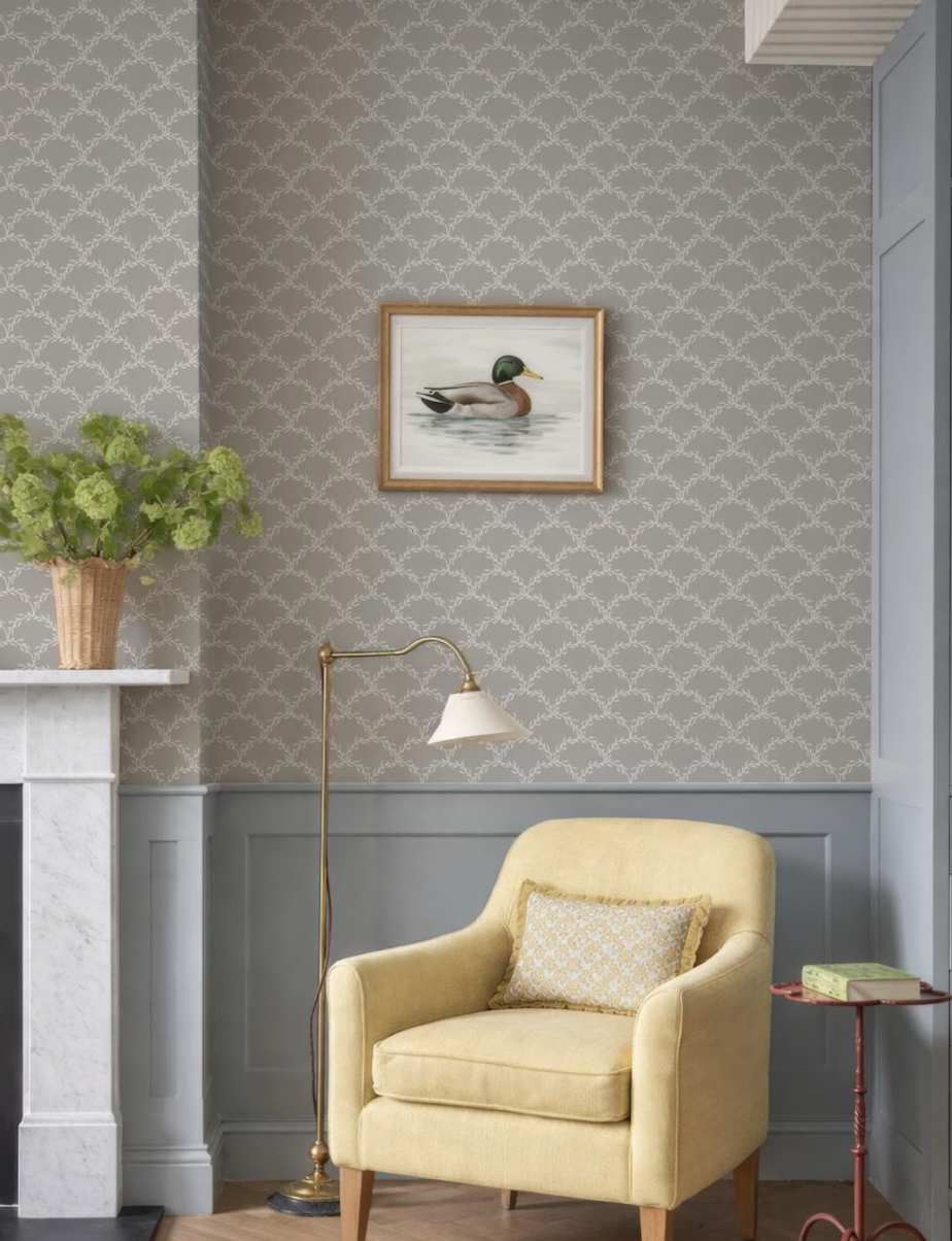 a cozy living room with a gray and white patterned wallpaper, a yellow armchair, a framed picture of a duck, a floor lamp, and a small side table with a book.