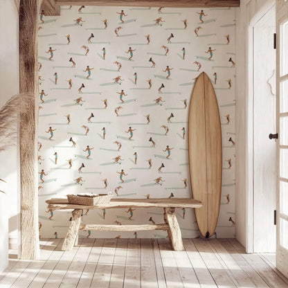 a wooden bench with a wicker basket on it, positioned in front of a wall with a repeating pattern of surfers riding waves. A surfboard is leaning against the wall next to the bench.