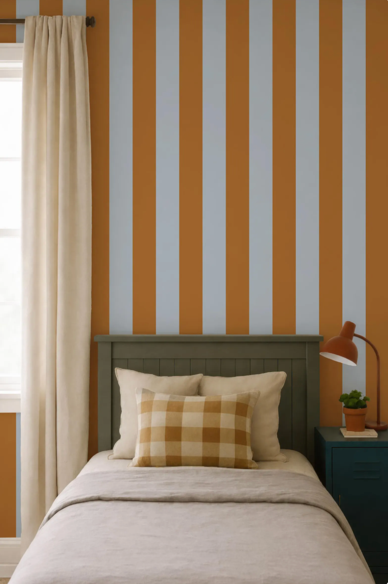 a bedroom with a bed, a nightstand, and a striped wall behind the bed. The bed has a checkered pillow and a lamp on the nightstand.