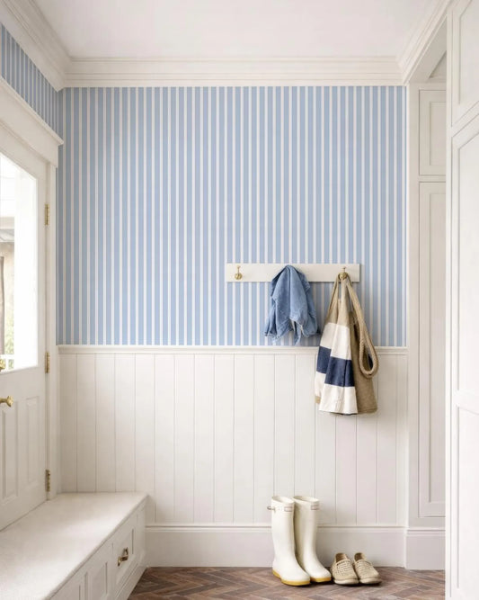 a well-organized entryway with a white bench, a coat rack with a jacket and a bag, and a pair of white rain boots. The walls are covered in blue and white striped wallpaper, and the floor is made of wood.