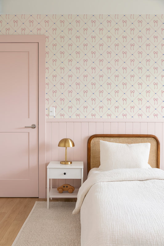 a cozy bedroom with a pink door, a white bed with a wooden headboard, and a white nightstand with a lamp. The walls are covered in a patterned wallpaper with pink and white bows.