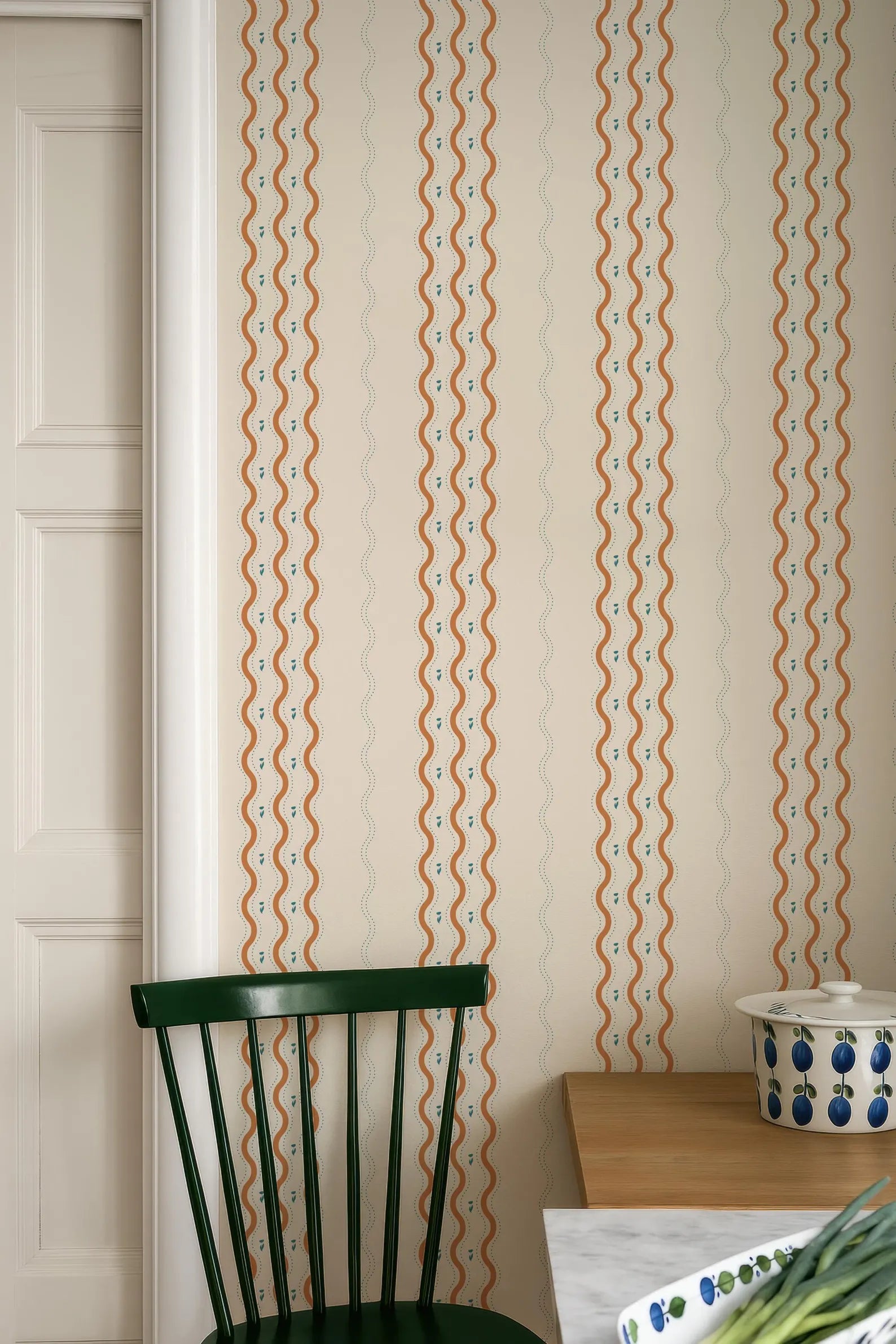 a kitchen interior with a green chair, a wooden table, and a patterned wall behind it.
