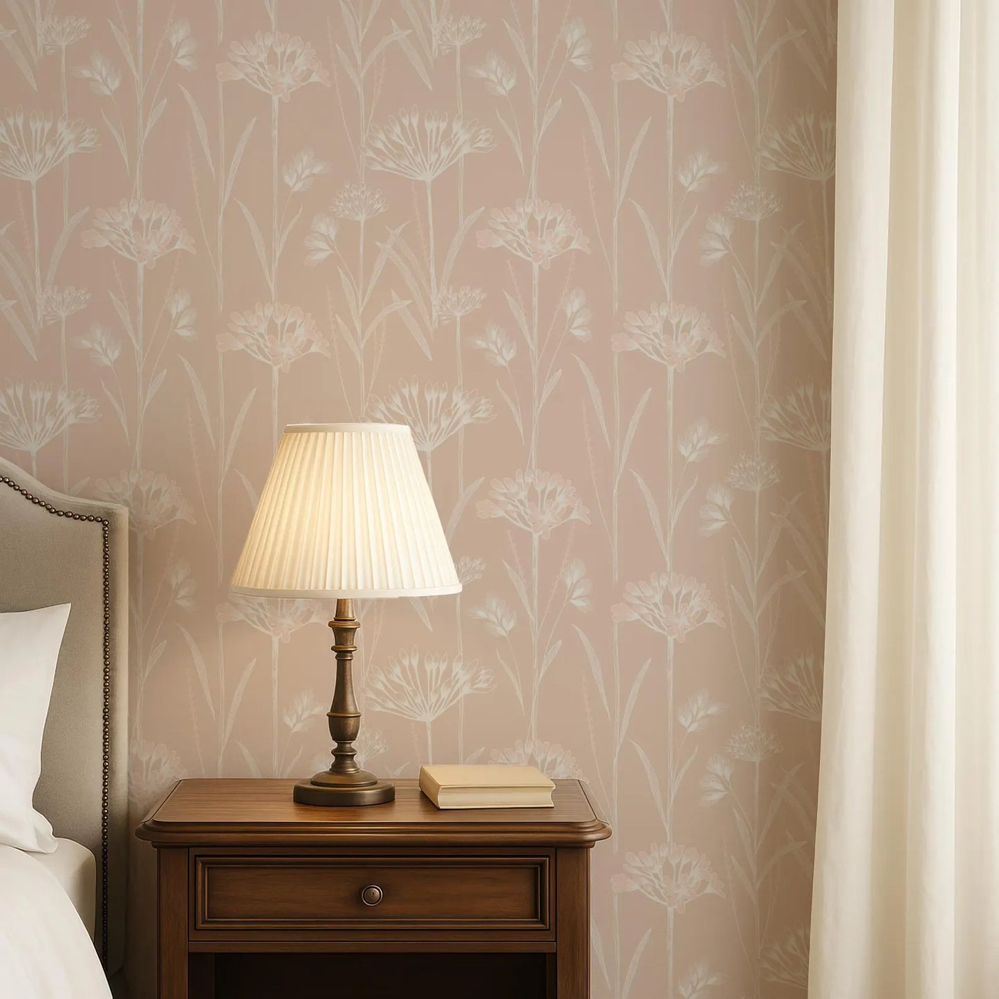 a bedroom setting with a wooden nightstand, a lamp, and a book. The lamp has a white shade and is placed on the nightstand. The wall behind the nightstand has a floral wallpaper pattern.