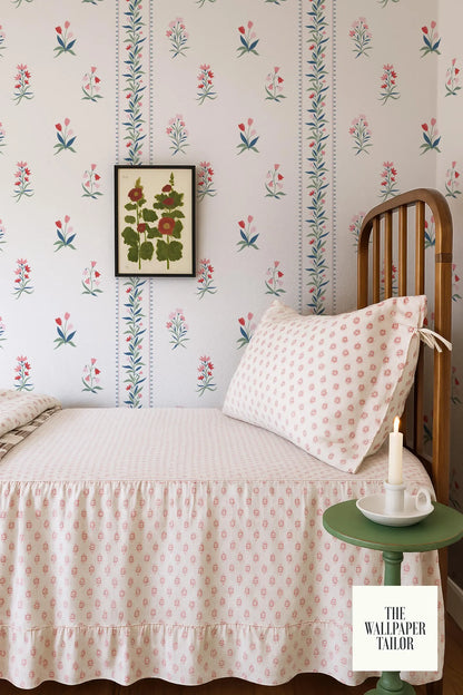 a bedroom with a floral wallpaper pattern, a wooden headboard, and a white bedspread with a pink and white polka dot design. There is a framed picture hanging on the wall above the bed, and a small table with a candle on it next to the bed.