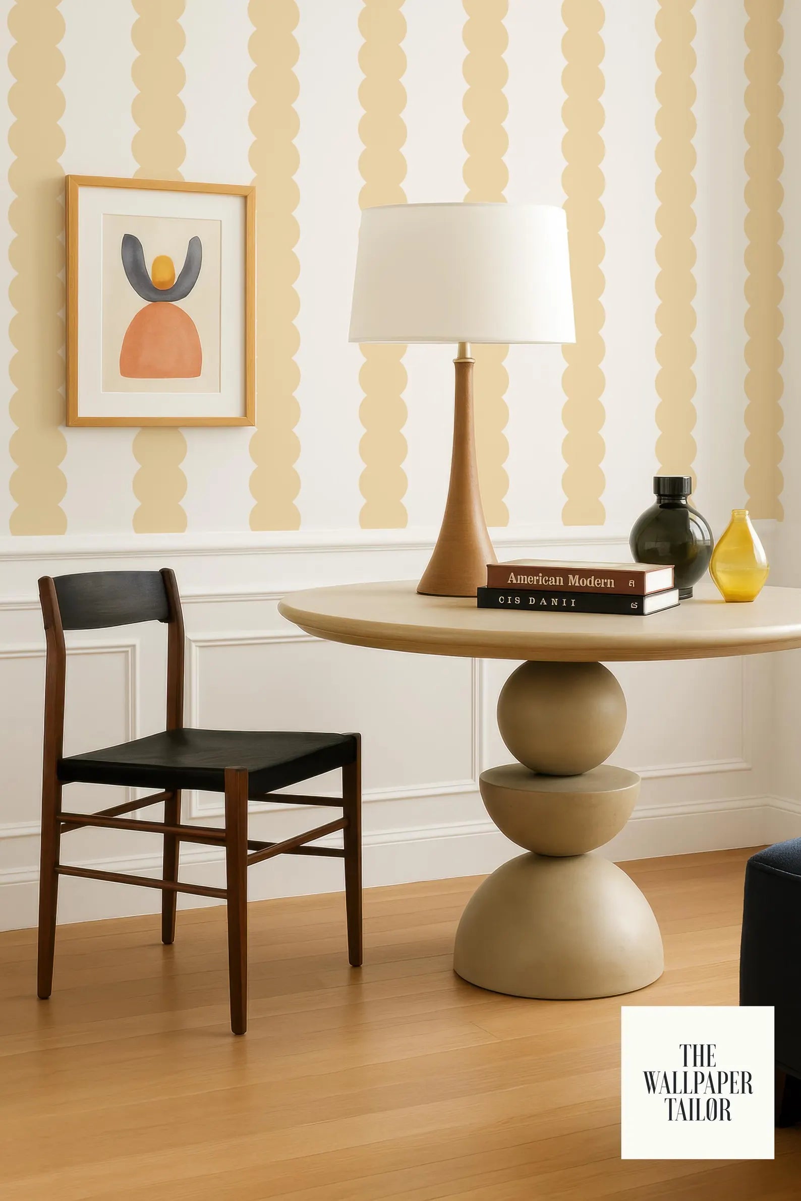 a modern and stylish living room with a wooden chair, a round table with a lamp, and a framed artwork on the wall.