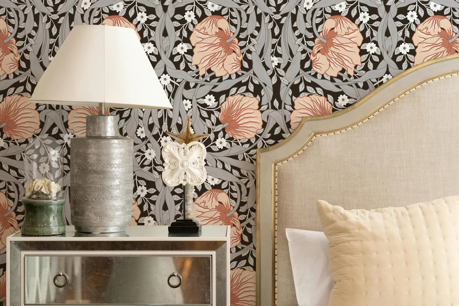 a bedroom with a floral wallpaper, a white headboard, a silver lamp, and a white dresser with a mirror.