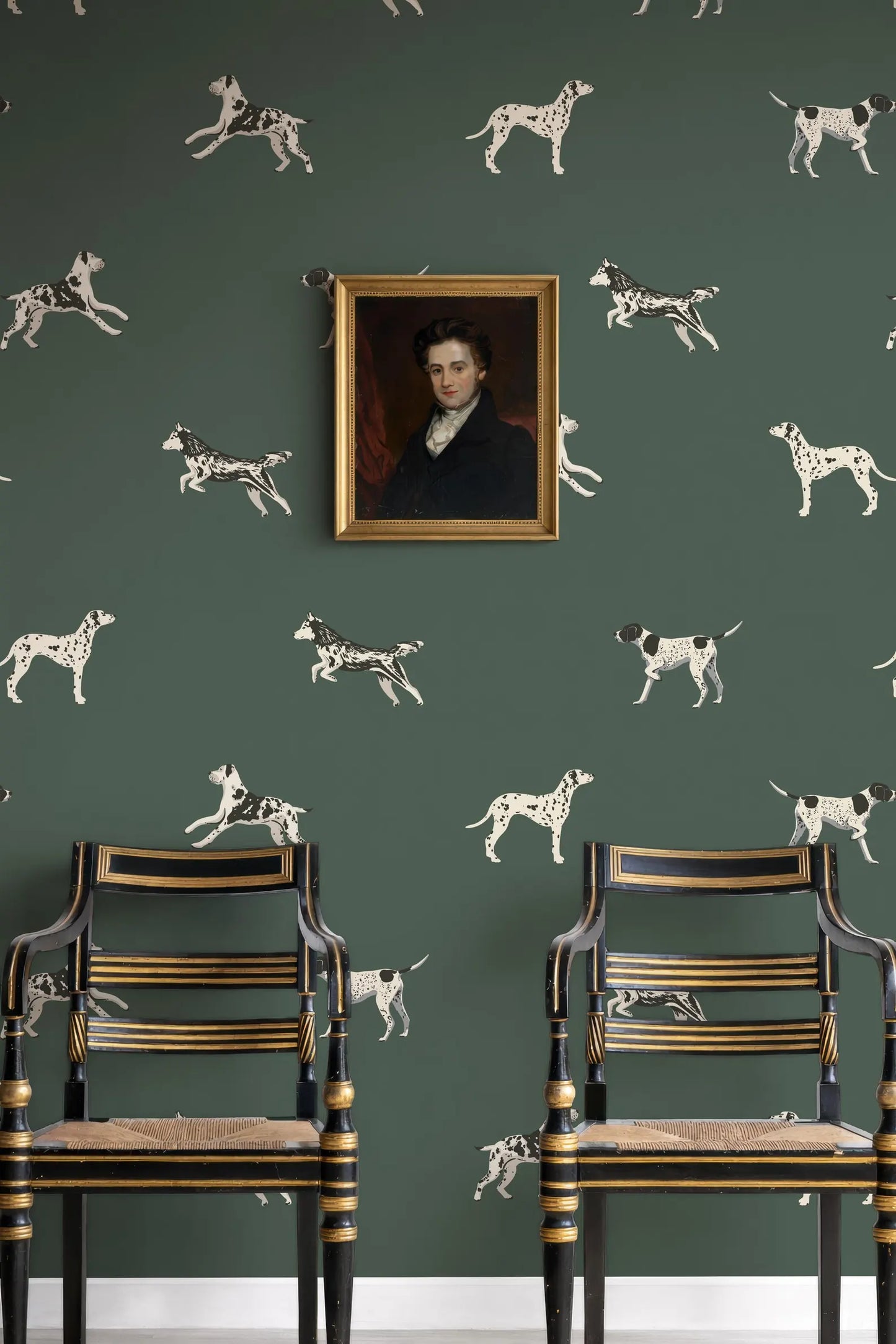 a green wall with a framed portrait of a man hanging above two antique chairs with gold trim.