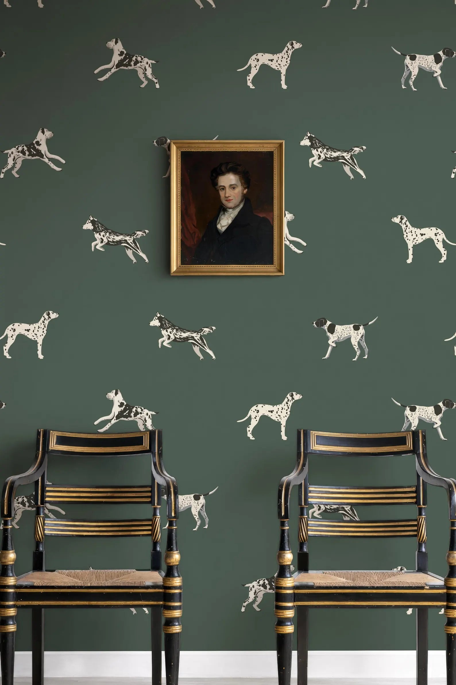 a green wall with a framed portrait of a man hanging above two antique chairs with gold trim.