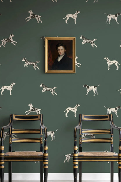 a green wall with a framed portrait of a man hanging above two antique chairs with gold trim.