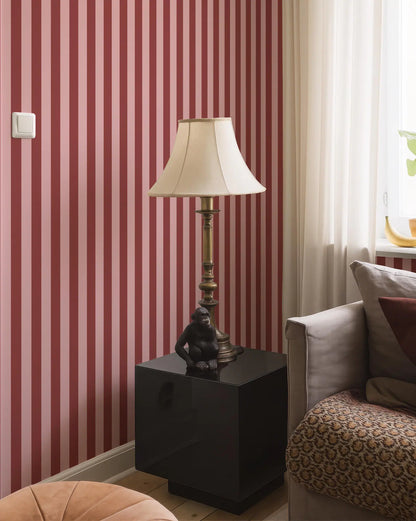 a living room with a red and white striped wallpaper, a black lamp on a black side table, a gray sofa, and a gold-colored vase on a windowsill.