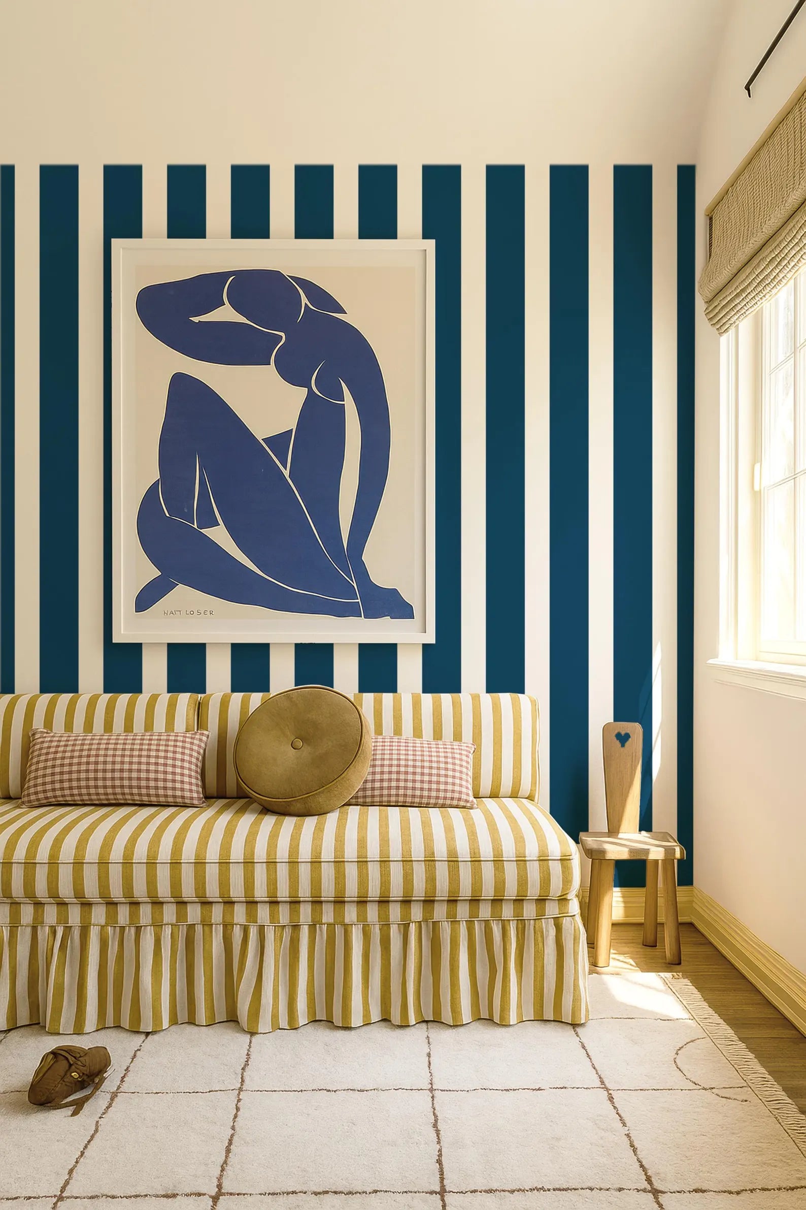 a living room with a striped sofa, a framed artwork of a woman, and a wooden stool. The room has blue and white striped walls, and a rug is visible on the floor.