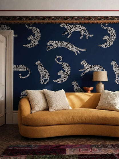 a living room with a yellow sofa and a patterned wallpaper with white leopard designs on a dark blue background.