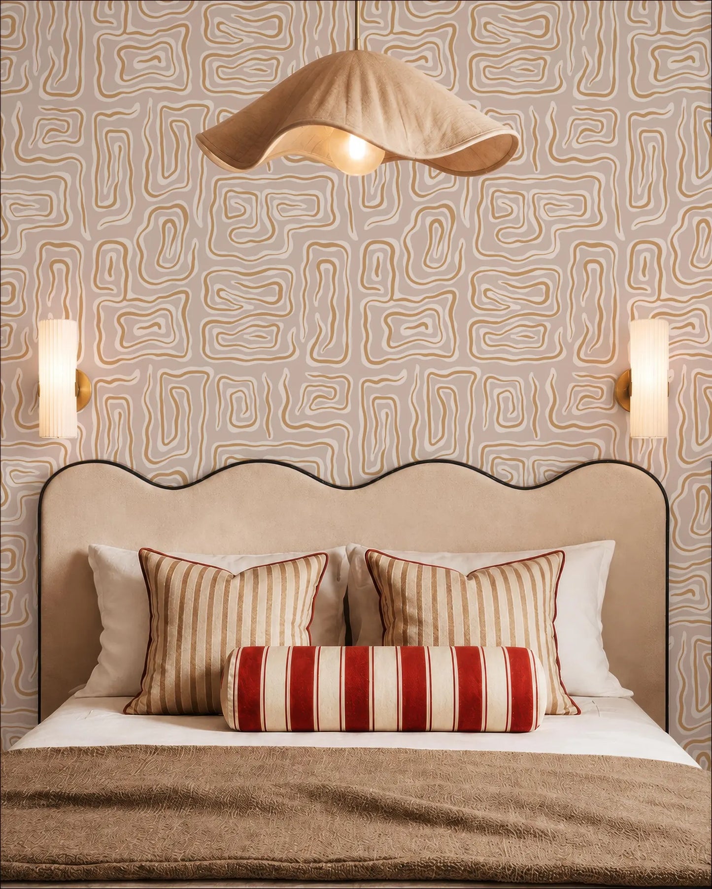 a well-decorated bedroom with a large bed, a beige headboard, and a patterned wallpaper. The bed is adorned with striped pillows and a red and white striped pillowcase. Above the bed, there is a beige pendant light hanging from the ceiling. The walls are covered in a geometric patterned wallpaper, and there are two wall sconces on either side of the bed.