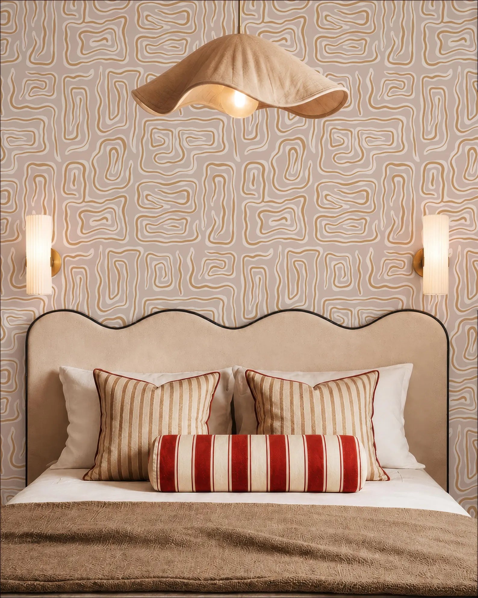 a well-decorated bedroom with a large bed, a beige headboard, and a patterned wallpaper. The bed is adorned with striped pillows and a red and white striped pillowcase. Above the bed, there is a beige pendant light hanging from the ceiling. The walls are covered in a geometric patterned wallpaper, and there are two wall sconces on either side of the bed.