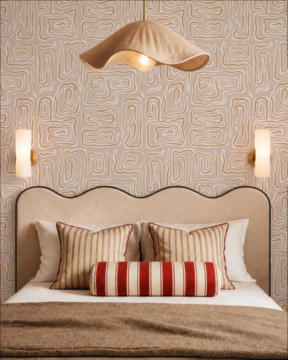 a well-decorated bedroom with a large bed, a beige headboard, and a patterned wallpaper. The bed is adorned with striped pillows and a red and white striped pillowcase. Above the bed, there is a beige pendant light hanging from the ceiling. The walls are covered in a geometric patterned wallpaper, and there are two wall sconces on either side of the bed.