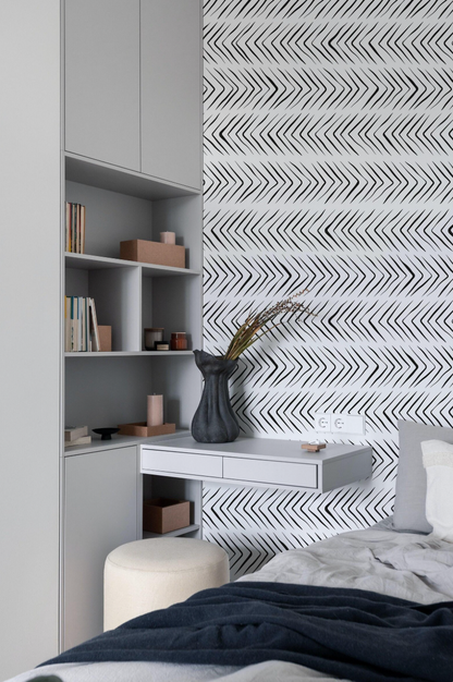 a modern bedroom with a white bookshelf, a black vase with greenery, and a gray and white zigzag patterned wallpaper.