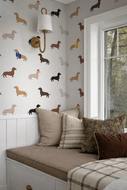 a wallpapered wall with a pattern of dachshunds in various colors and sizes, creating a playful and whimsical atmosphere. The wall is complemented by a white lamp and a window, which allows natural light to illuminate the space. The room is furnished with a couch and a bed, both adorned with decorative pillows, adding to the cozy and inviting ambiance.