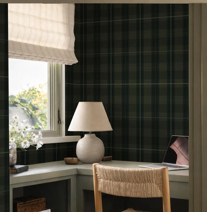 a cozy workspace with a desk, a lamp, and a laptop, all situated near a window with a white shade.