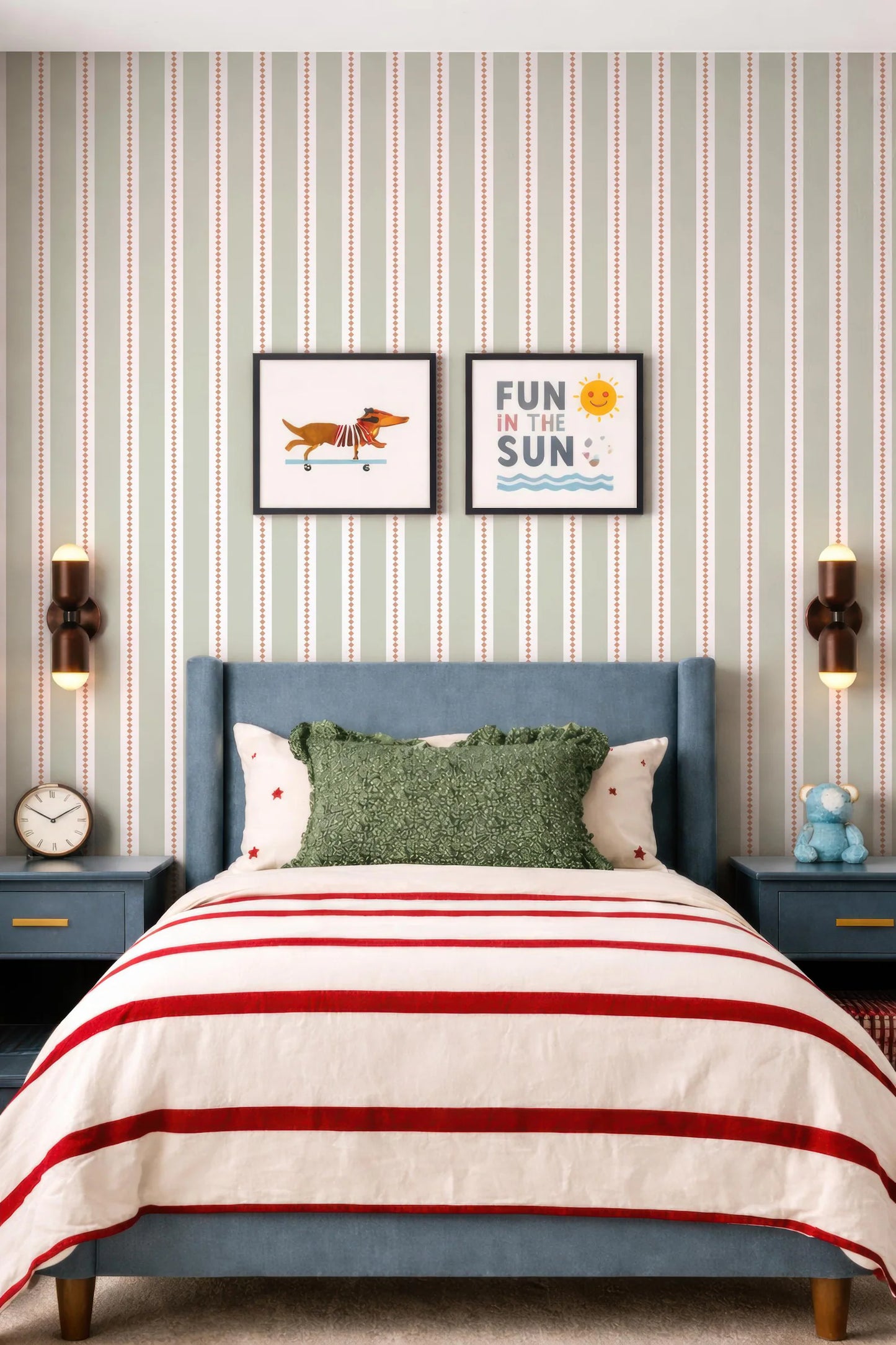 a bedroom with a blue headboard and a striped comforter. Above the bed, there are two framed pictures on the wall, one depicting a dog and the other with the text "Fun in the Sun". The room also has a clock on the wall and a stuffed animal on a nightstand.
