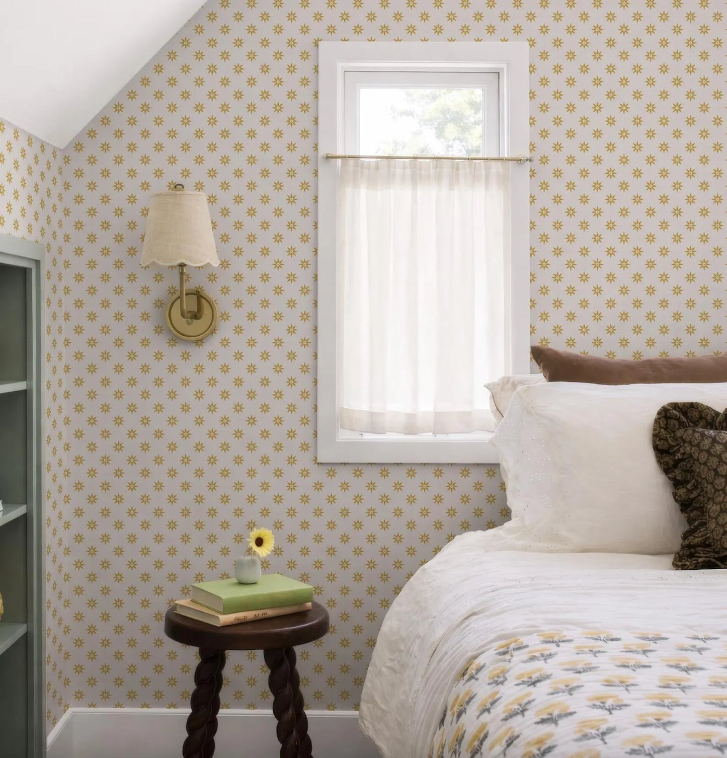 a cozy bedroom with a bed, a small table with a vase of flowers, and a window with a white curtain.