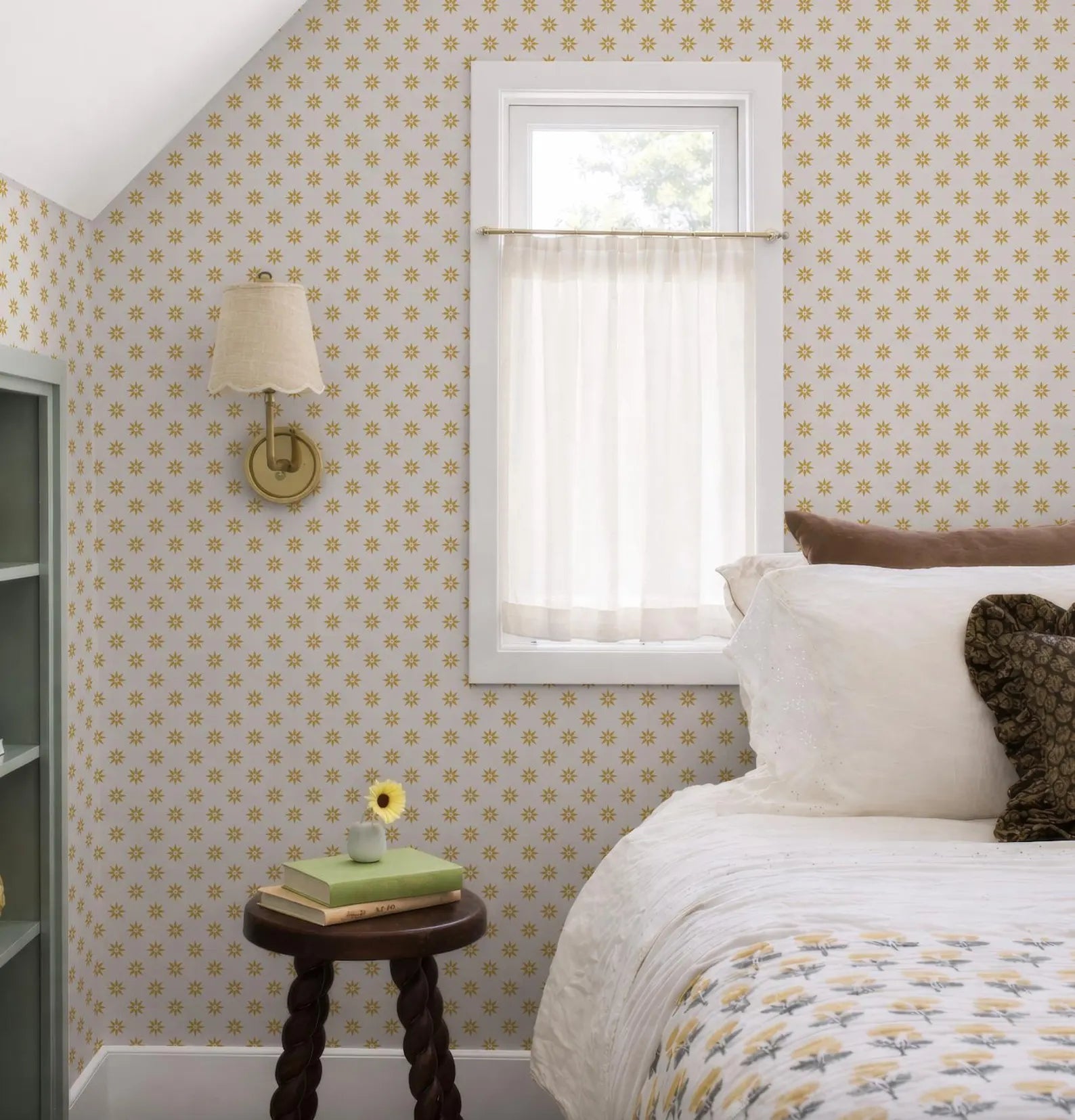 a cozy bedroom with a bed, a small table with a vase of flowers, and a window with a white curtain.