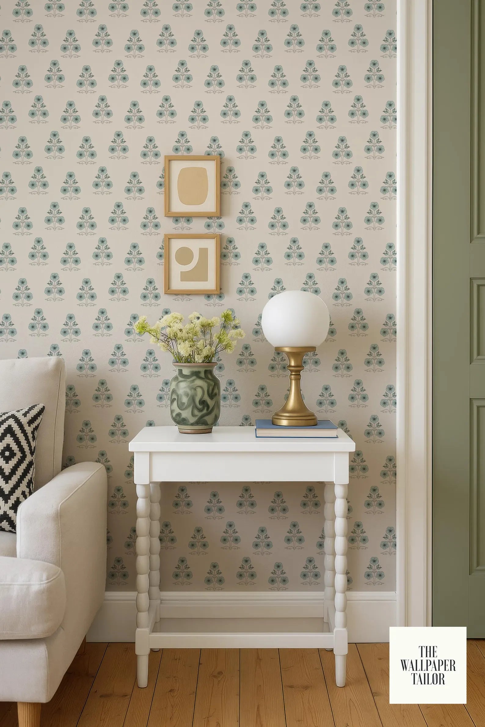 a cozy living room with a white sofa, a white side table with a lamp and a vase of flowers, and a patterned wallpaper.