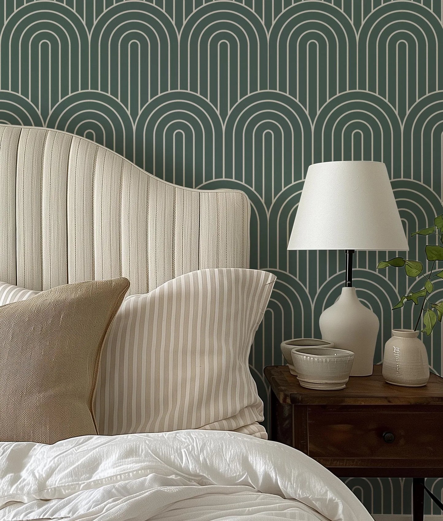 a bedroom with a bed, a nightstand, and a lamp. The bed has a white headboard and a striped pillow. The nightstand has a lamp and a small bowl on it. The wall behind the bed has a repeating pattern of arches in shades of green and white.