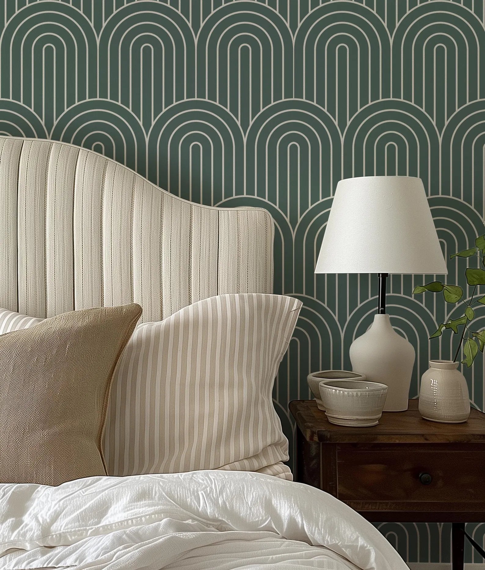 a bedroom with a bed, a nightstand, and a lamp. The bed has a white headboard and a striped pillow. The nightstand has a lamp and a small bowl on it. The wall behind the bed has a repeating pattern of arches in shades of green and white.