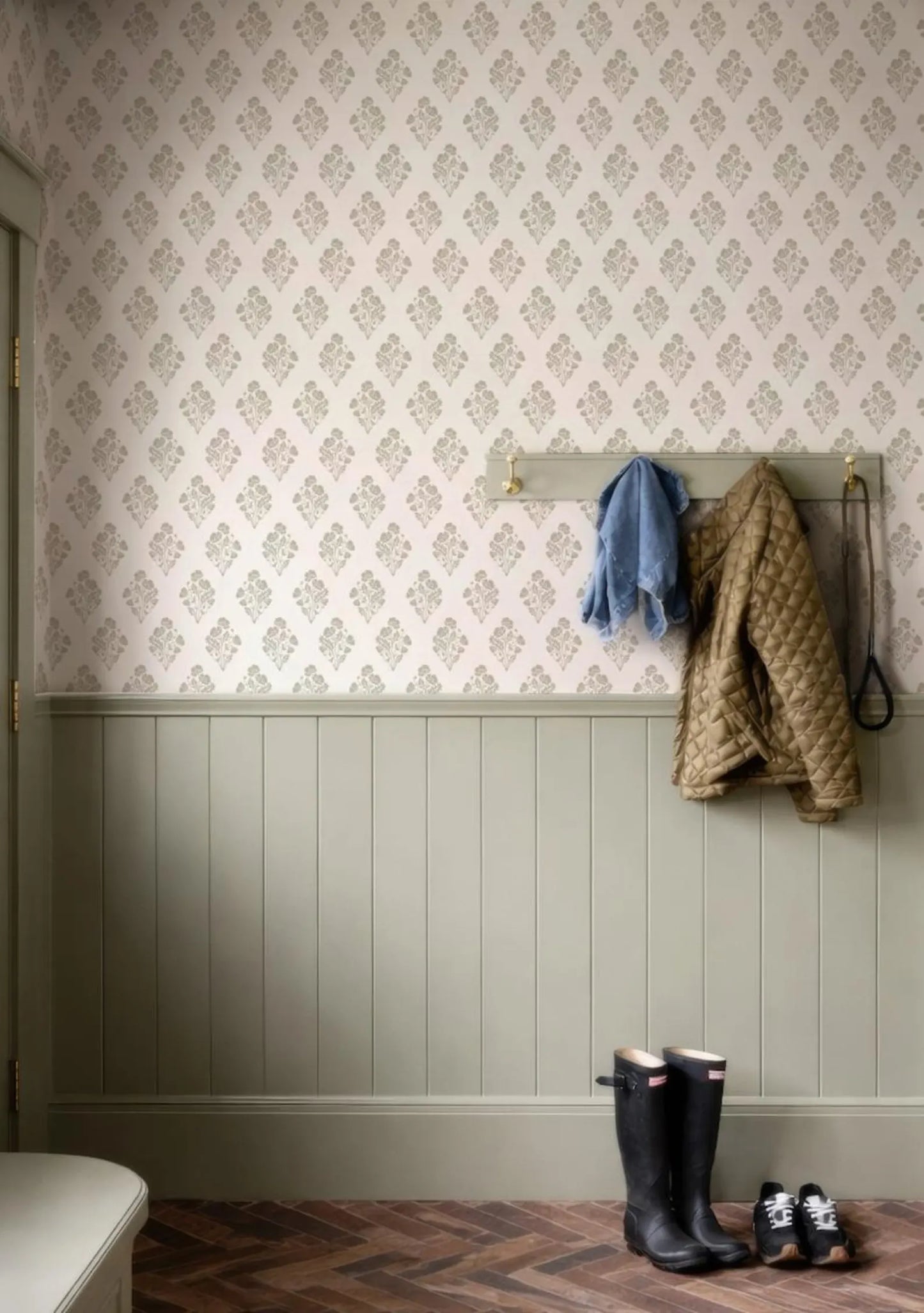 a hallway with a patterned wallpaper, a coat rack with jackets hanging on it, and a pair of black rain boots placed on the floor.