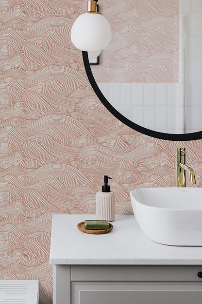 a bathroom with a white sink, a round mirror, and a pink and white wallpaper pattern. There is a soap dispenser and a small wooden tray on the countertop.