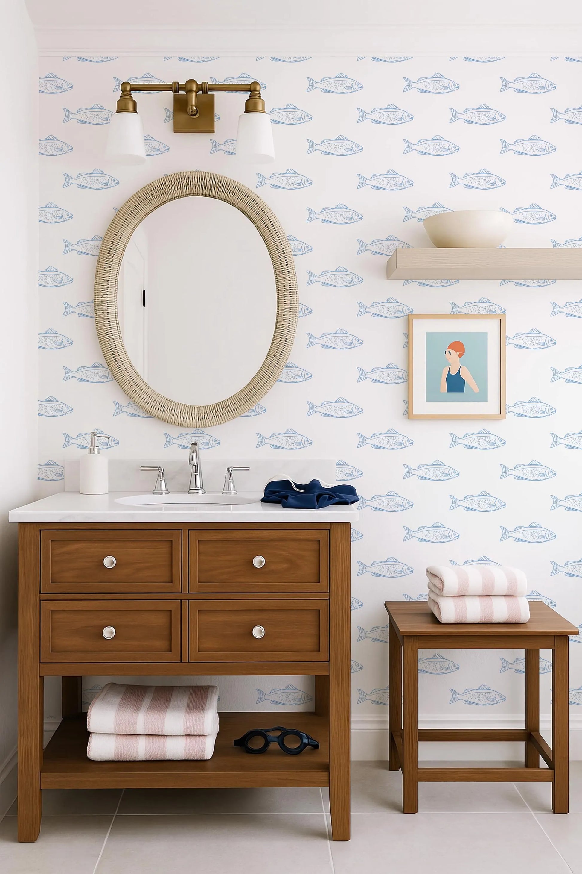 a bathroom with a wooden vanity, a round mirror, and a framed picture of a woman. The walls are decorated with a blue and white fish wallpaper, and there is a shelf with a bowl and a towel.