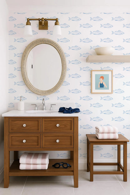 a bathroom with a wooden vanity, a round mirror, and a framed picture of a woman. The walls are decorated with a blue and white fish wallpaper, and there is a shelf with a bowl and a towel.