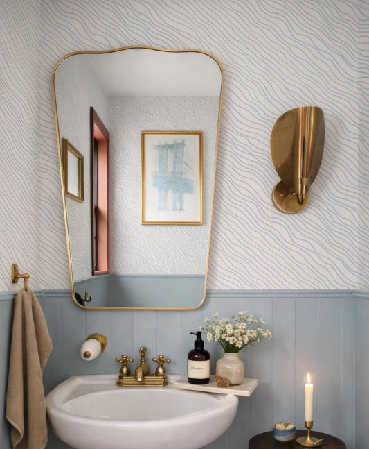 a bathroom with a white sink, a mirror, and a candle on a small table. The bathroom has a blue and white color scheme, and there is a painting on the wall.