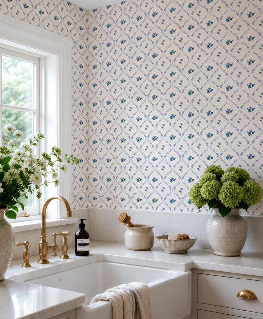 a well-organized kitchen with a white sink, a vase of green hydrangeas, and a bottle of soap on the counter. The walls are adorned with a blue and white floral wallpaper, and there is a window above the sink.
