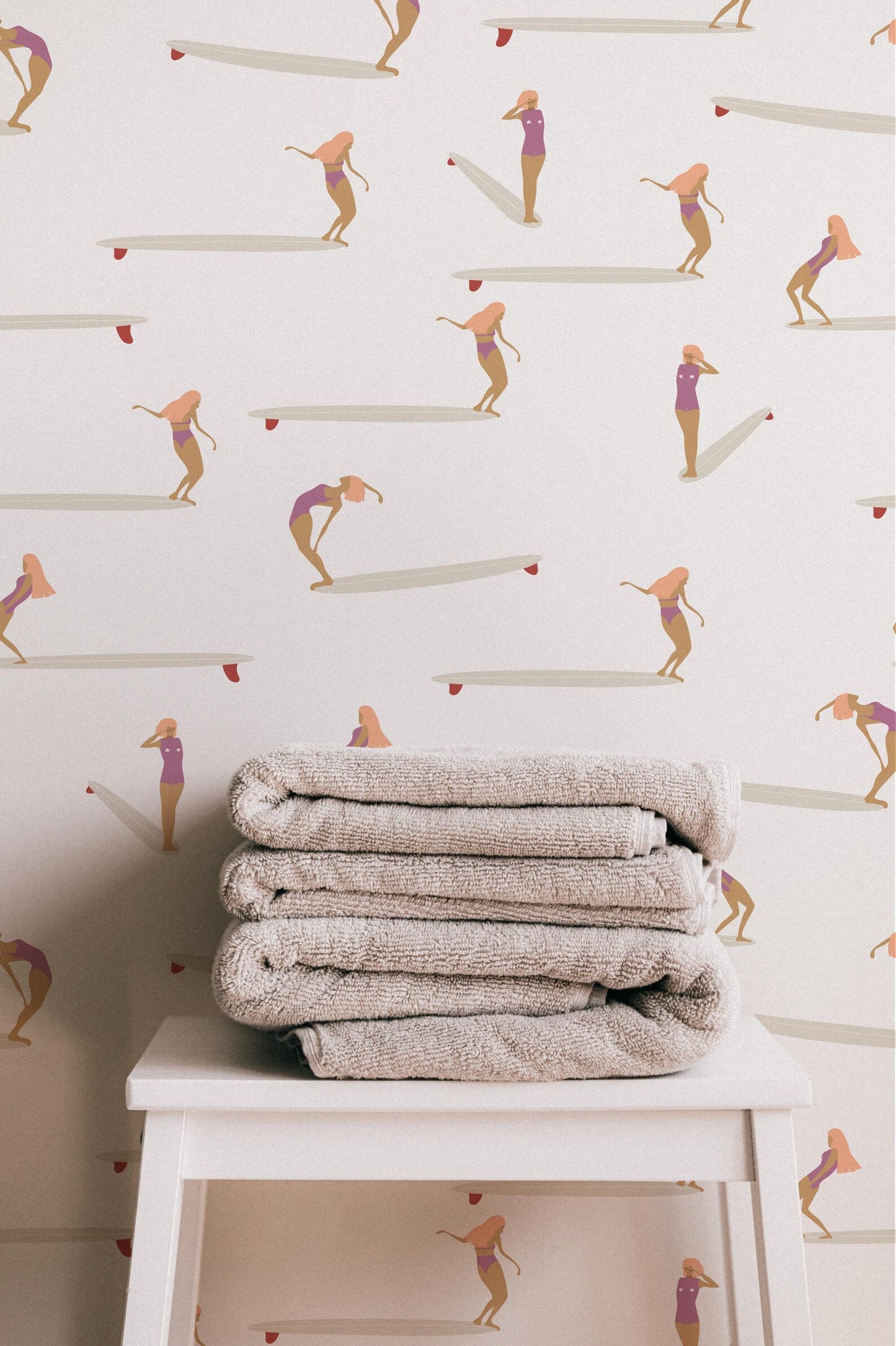 a stack of folded towels placed on a white table against a wall with a repeating pattern of surfers in pink and white outfits.