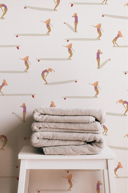 a stack of folded towels placed on a white table against a wall with a repeating pattern of surfers in pink and white outfits.