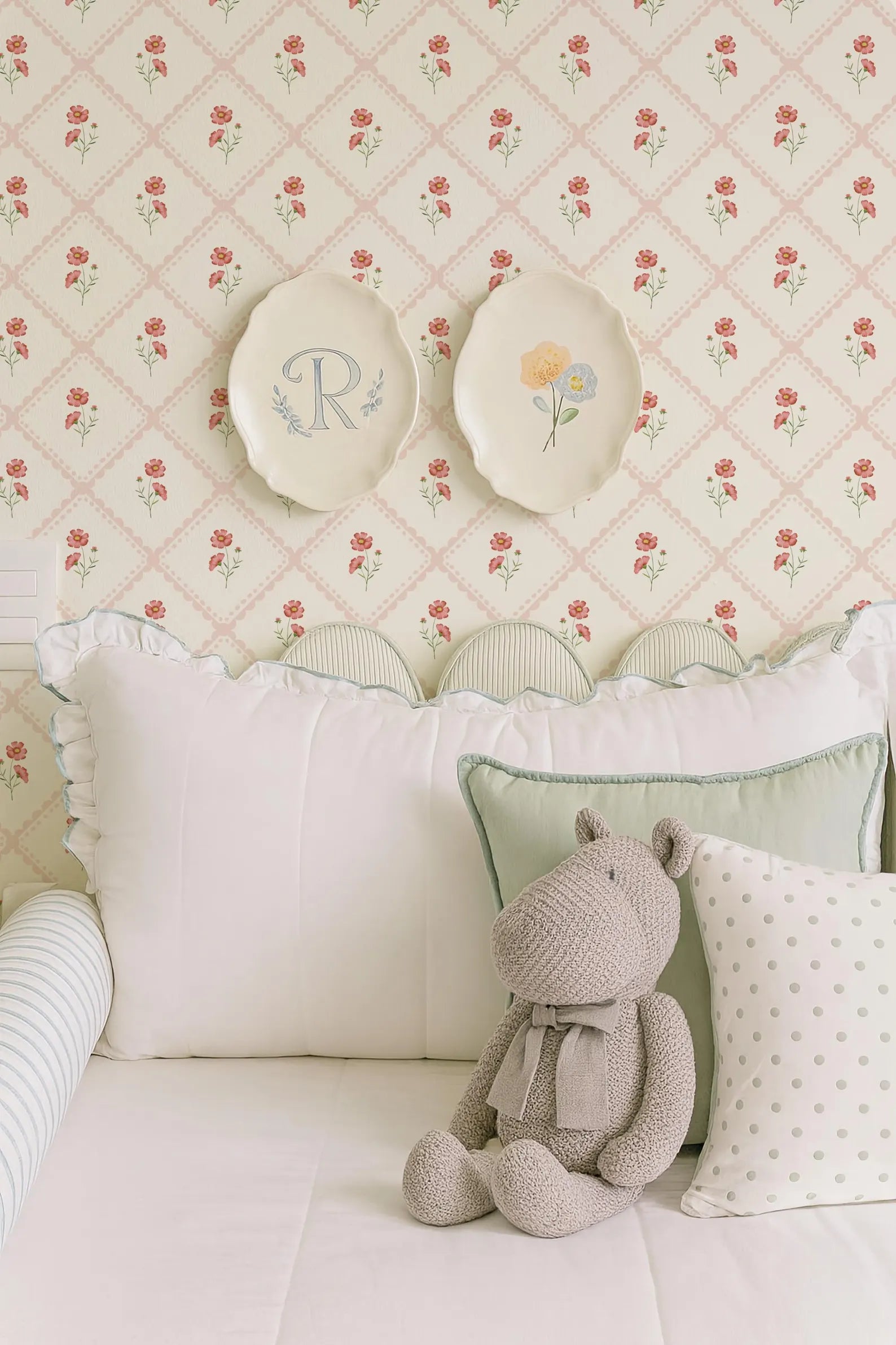 a cozy bedroom scene with a plush teddy bear sitting on a bed, surrounded by decorative pillows and a floral wallpaper.