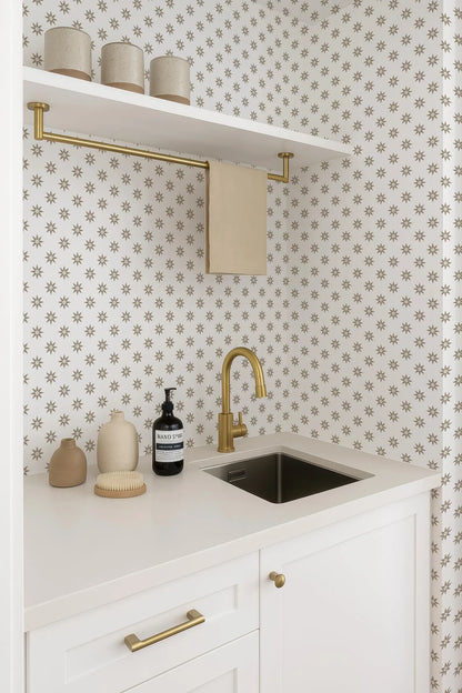 a bathroom with a white countertop, a sink, and a shelf above it. On the countertop, there are three vases and a bottle. The wall behind the countertop has a pattern of small white stars.