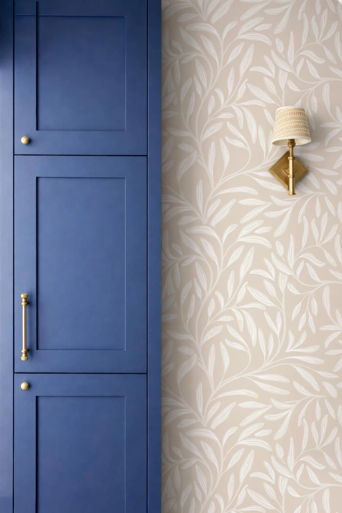 a blue cabinet door and a wallpapered wall with a gold-colored lamp.