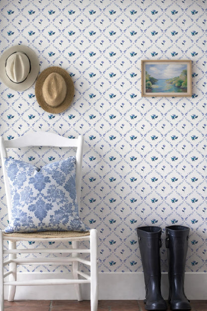 a cozy corner with a white chair, a pair of black rain boots, and a framed picture of a landscape on the wall. The chair has a blue and white floral pillow on it.