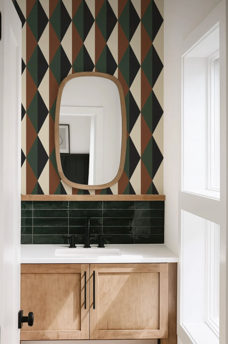 a bathroom with a white countertop, a black faucet, and a mirror above it. The walls are decorated with a geometric pattern in various colors, including green, brown, and black. The bathroom appears to be well-lit and clean, with a window providing natural light.