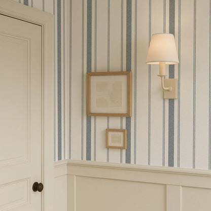 a wall with a striped wallpaper pattern, a framed picture, and a wall-mounted lamp.