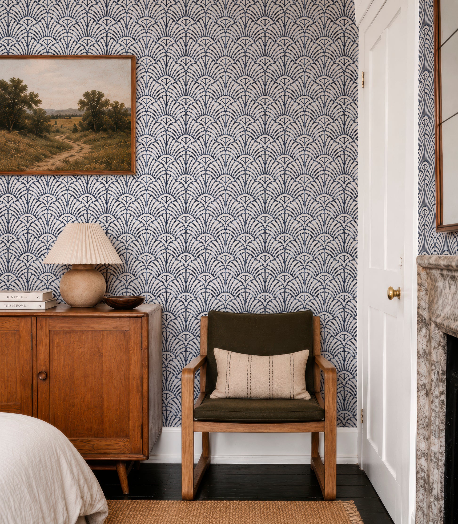a cozy bedroom with a wooden dresser, a green armchair, and a fireplace. The walls are covered in a patterned wallpaper, and there is a painting hanging above the dresser.