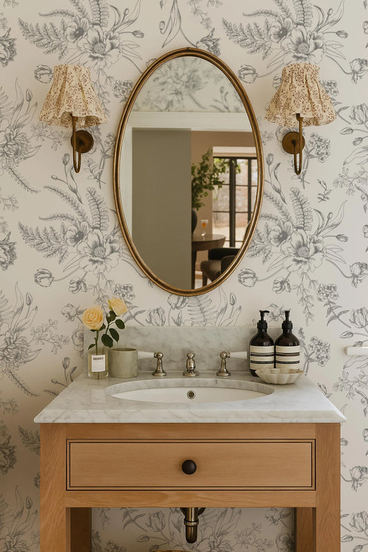 a bathroom sink with a marble countertop, a large oval mirror, and two wall sconces with floral-patterned lamps.