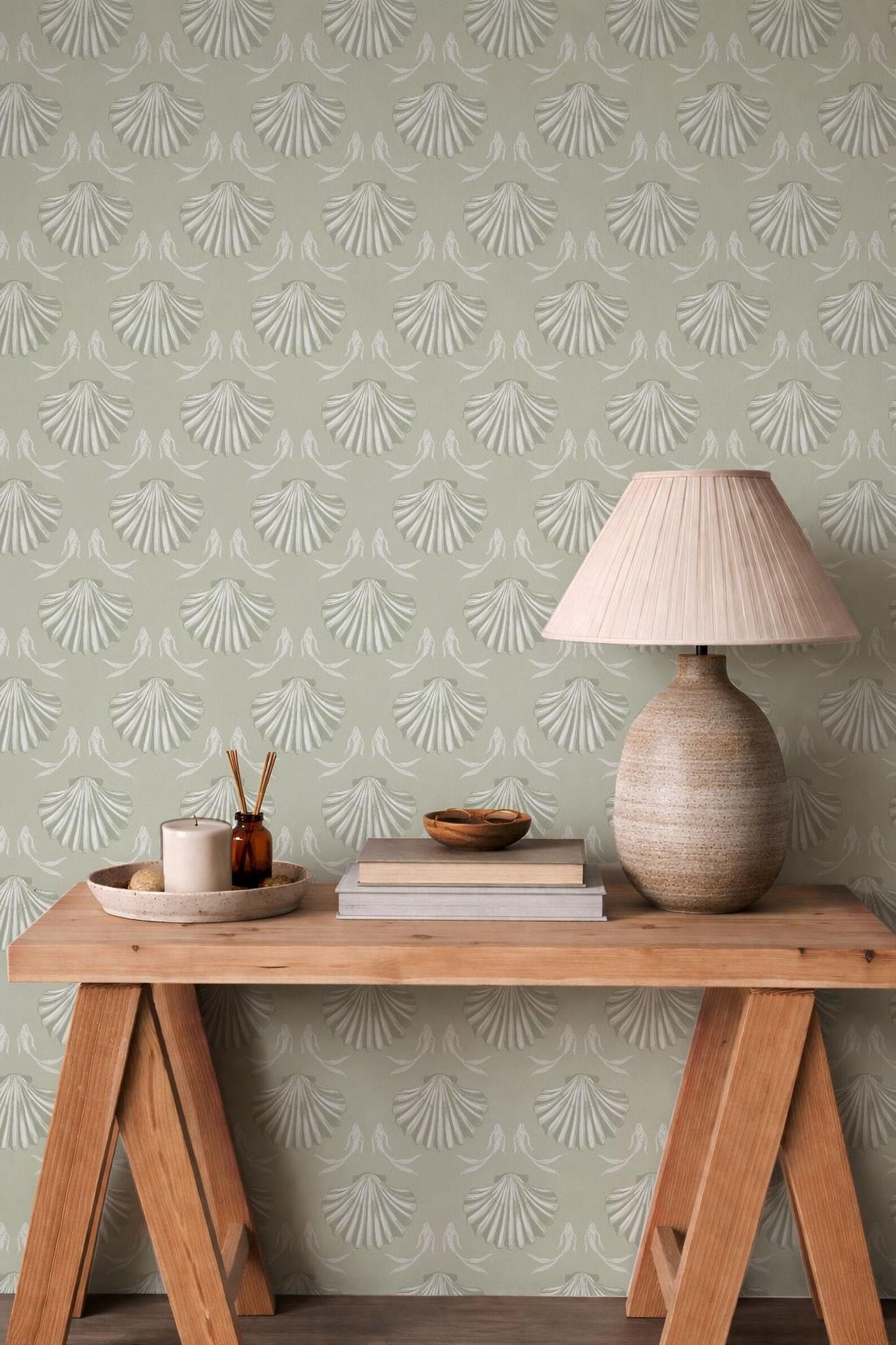 a wooden table with a lamp, a bowl, and a book on it, set against a wall with a repeating pattern of white and green leaves.
