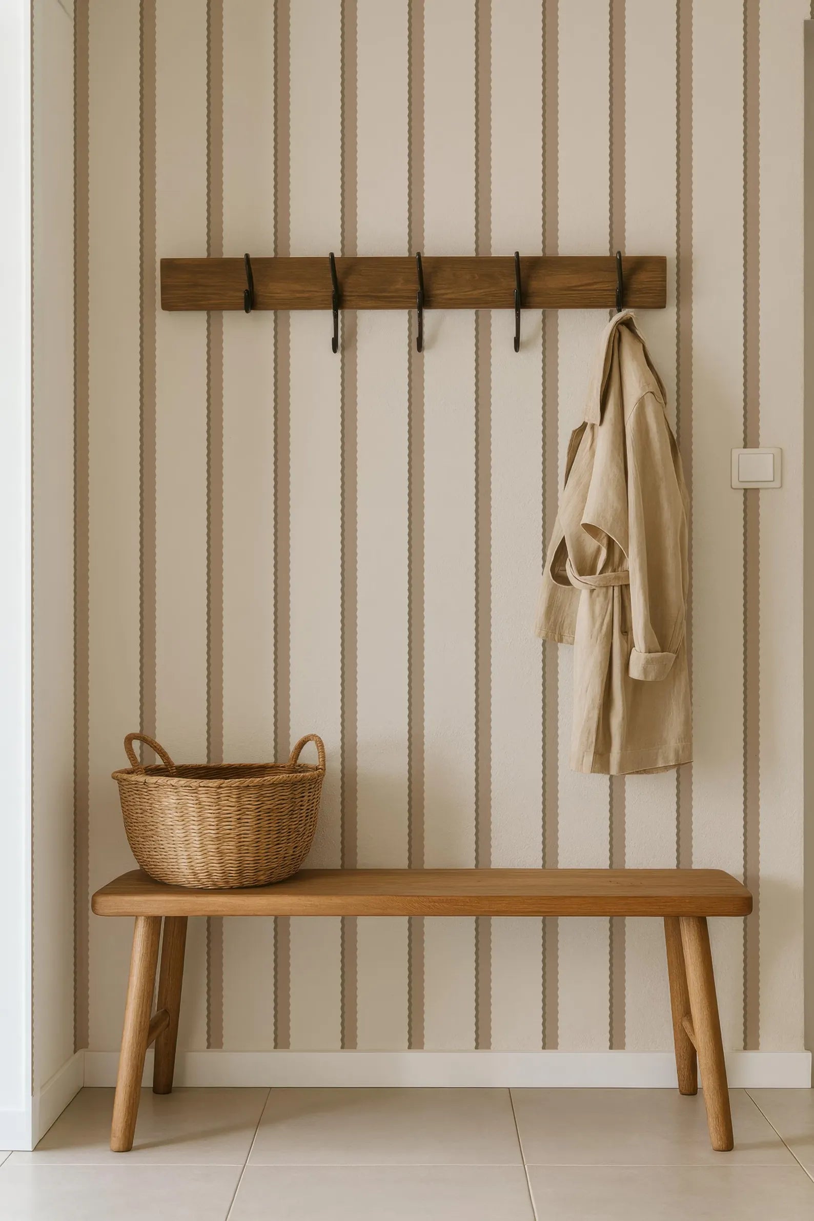 a wooden bench with a wicker basket on it, placed in a hallway with a striped wall and a coat rack above it.