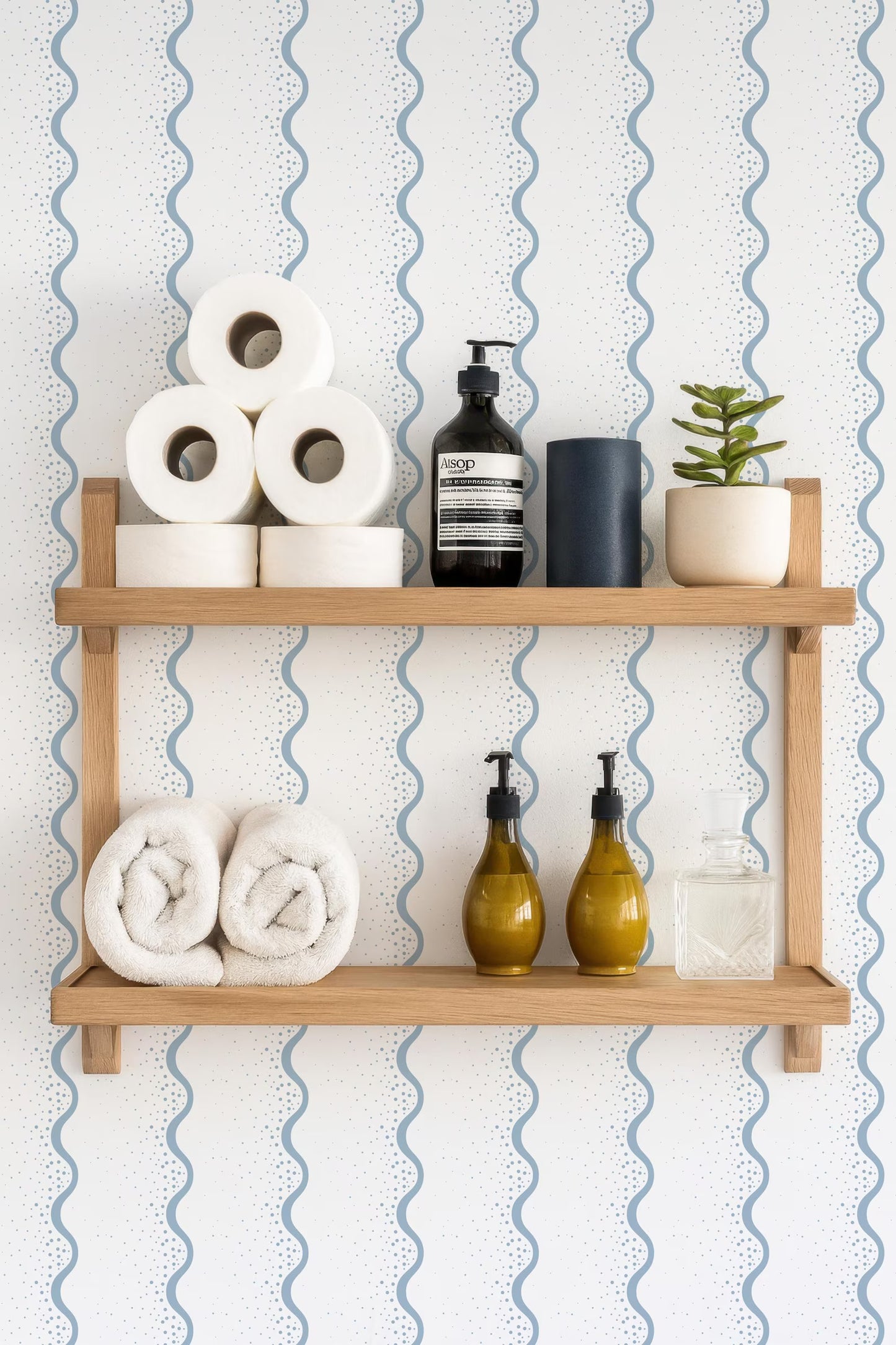a wooden shelf with various toiletries and decorative items, including rolled towels, a soap dispenser, a bottle of lotion, and a small potted plant.