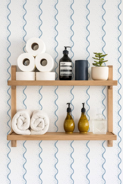 a wooden shelf with various toiletries and decorative items, including rolled towels, a soap dispenser, a bottle of lotion, and a small potted plant.