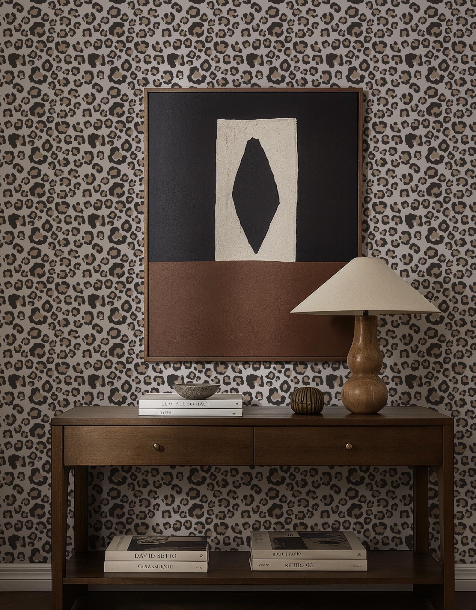 a wooden console table with a lamp, books, and a framed abstract artwork on a leopard print wallpaper.