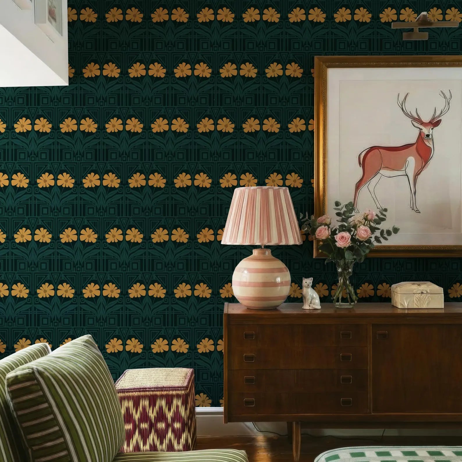 a living room with a green and gold patterned wallpaper, a wooden dresser with a lamp and a framed picture of a deer, a striped ottoman, and a green and white striped chair.